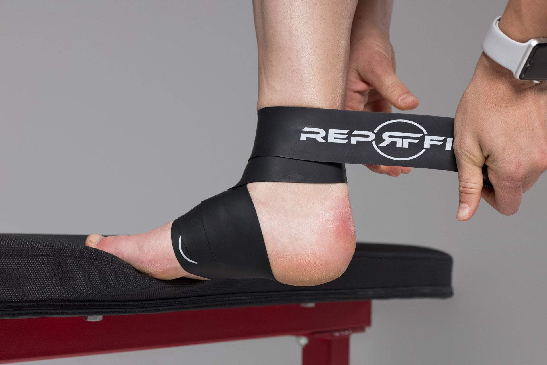Lifter wrapping a black REP floss band around her ankle.