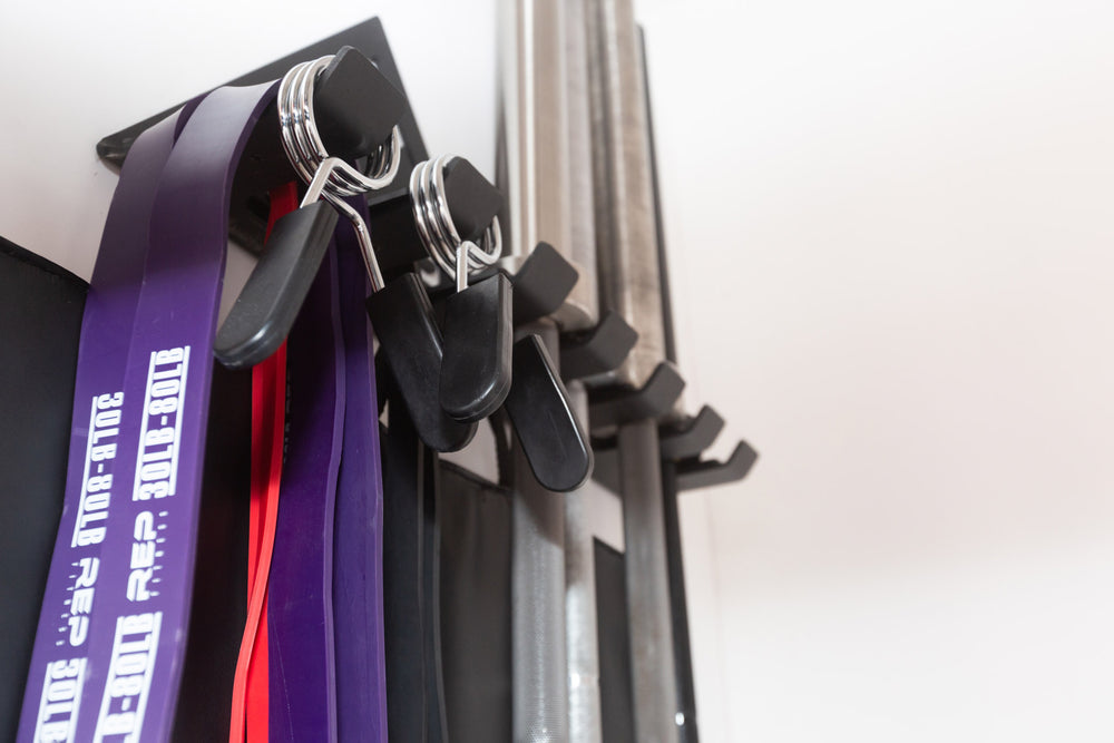 Close-up view of exercise bands, spring clips, and barbells all being stored on the REP Multi-Use Wall Storage.