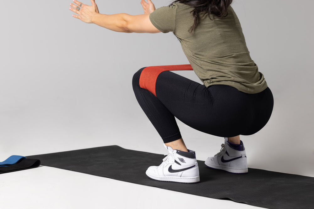 Lifter performing an air squat using the red light resistance REP circle hip band.