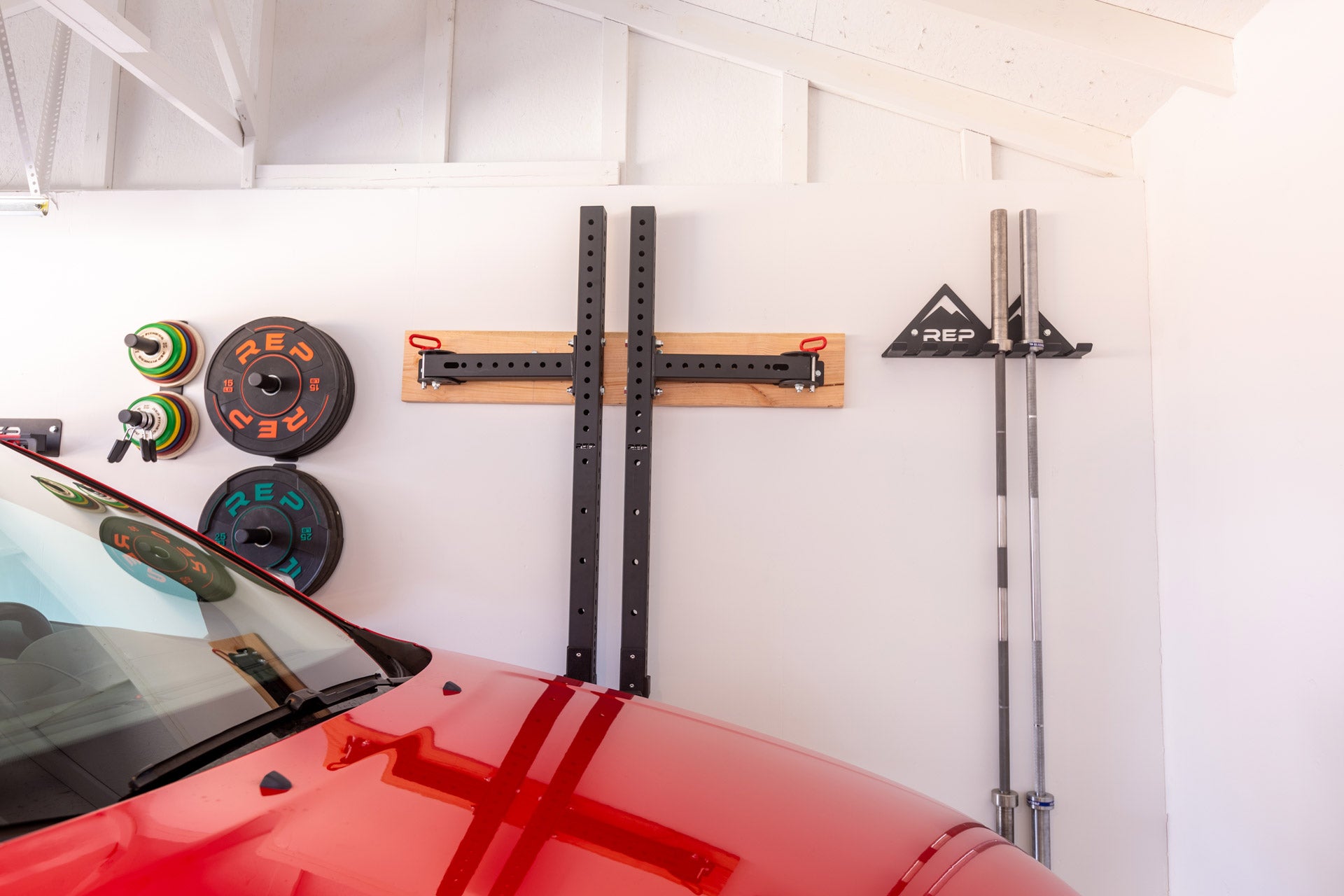A garage gym with a parked car in it showcasing a variety of REP space-saving equipment including single and double Wall Mounted Plate Storage.