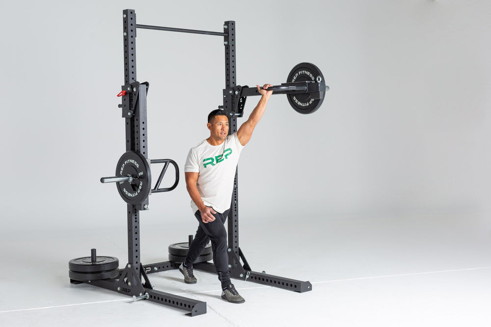 Lifter performing a single arm shoulder press using a REP Iso Arm attached to a REP Squat Rack and loaded with a 25lb Black Bumper Plate.