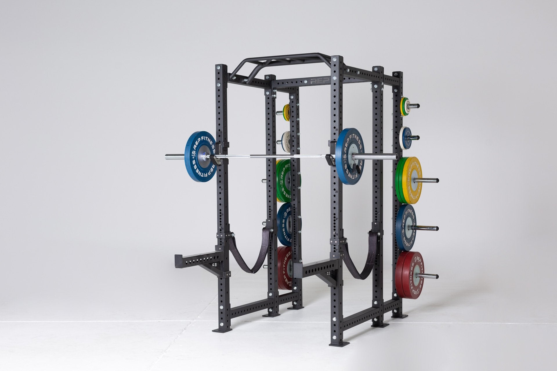 Full view of a REP 6-post PR-4000 power rack with green 25, yellow 35, blue 45, and red 55lb competition bumper plates on the weight horns, and a racked barbell loaded with blue 45lb competition bumper plates.