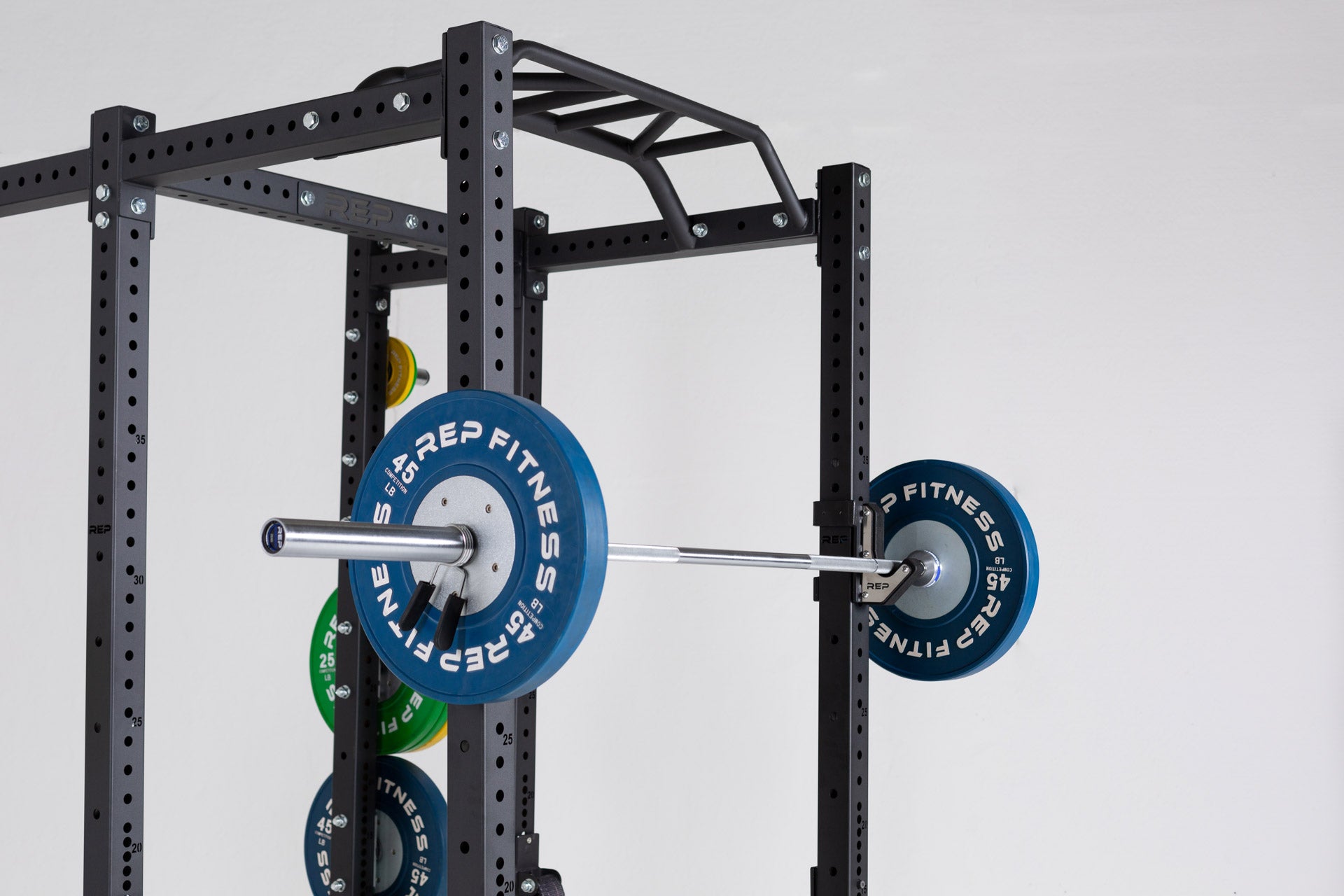 View of barbell loaded with a pair of blue 45lb competition bumper plates racked on a REP PR-4000 power rack.