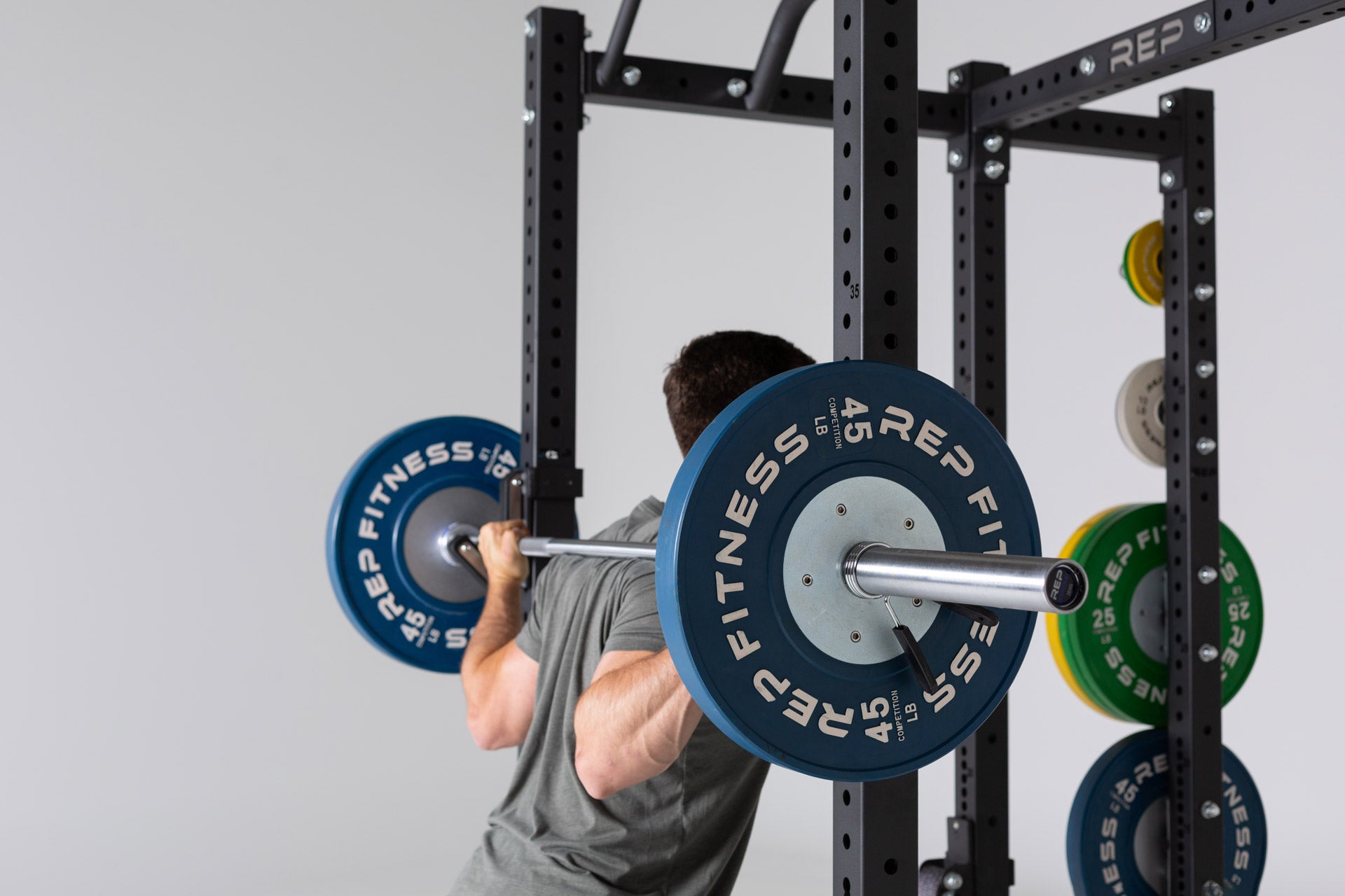 Close up view of a lifter preparing to unrack a barbell loaded with 45lb Competition Bumper Plates from the J-cups on a PR-4000 rack.
