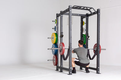 Lifter in the bottom of a front squat using a barbell loaded with a pair of 55lb Competition Bumper Plates inside of a PR-4000 rack with strap safeties attached.