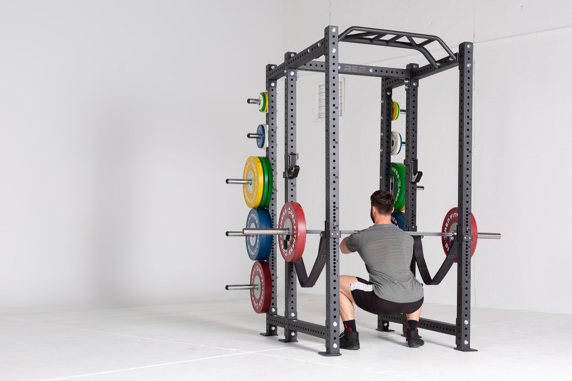 Lifter in the bottom of a front squat using a barbell loaded with a pair of 55lb Competition Bumper Plates inside of a PR-4000 rack with strap safeties attached.