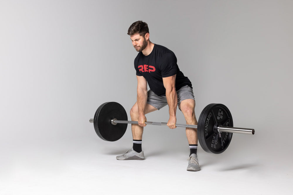 Lifter performing a sumo-stance deadlift at just below knee level position using a barbell loaded with two pairs of 45lb Old School Iron Plates and spring clips.