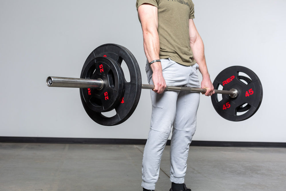 Lifter at the top position of a deadlift using a barbell loaded with a pair of 45lb and 25lb Rubber Coated Olympic Plates.